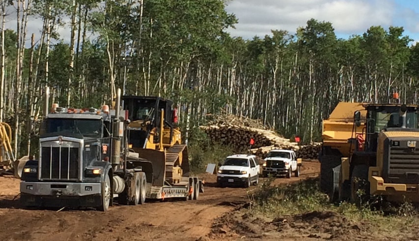 Site clearing equipment leaving the site on the north bank of the Site C dam site, with log stock pile in the background.