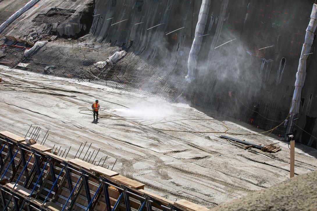 A worker sprays mist on the roller-compacted concrete surface before the next layer of concrete is placed. | May 2021