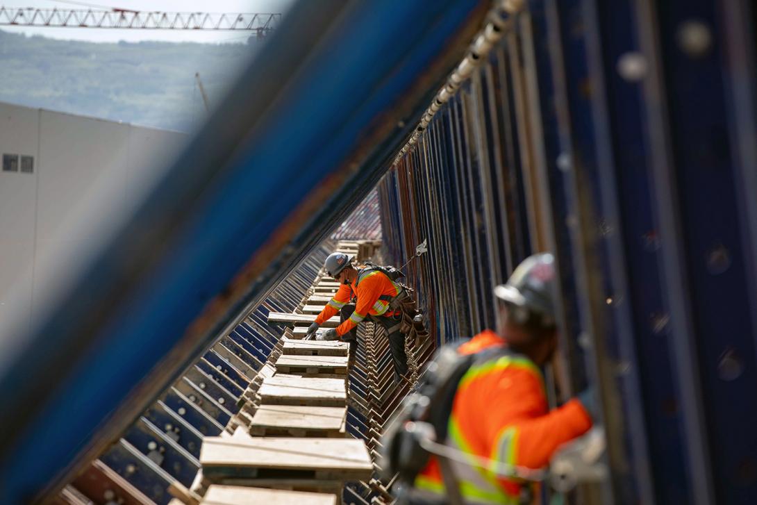 Workers install roller-compacted concrete formwork between reinforced steel on the dam buttress. The distance between the blue cantilever supports is approximately 90 centimetres. | June 2021