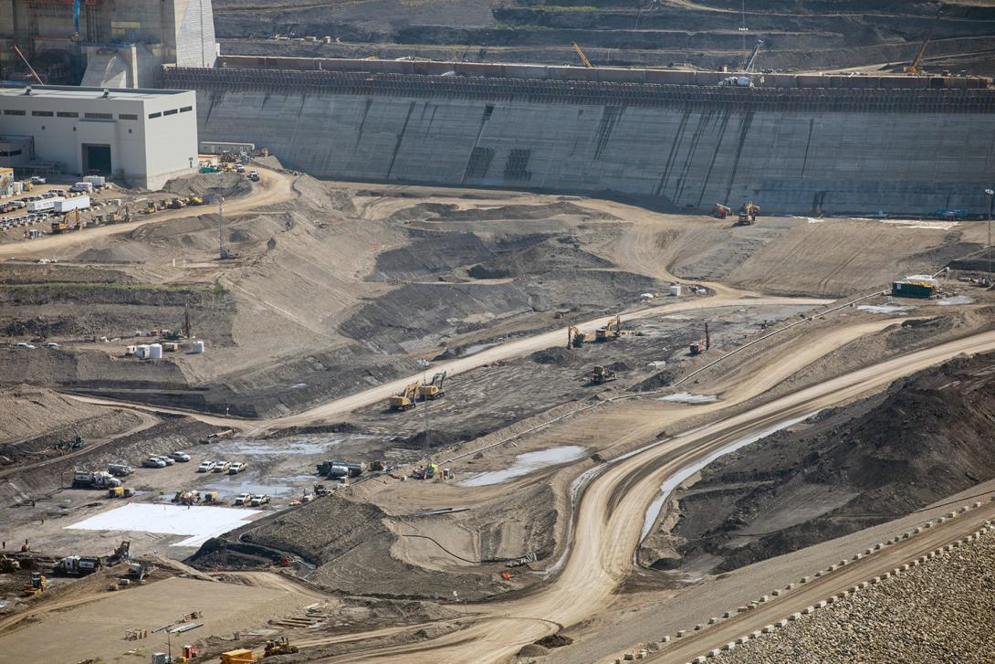 Aggregate material is filtered and placed in the dam’s downstream shell. At centre, the top layer is removed to access the bedrock layer in the core trench. | July 2021