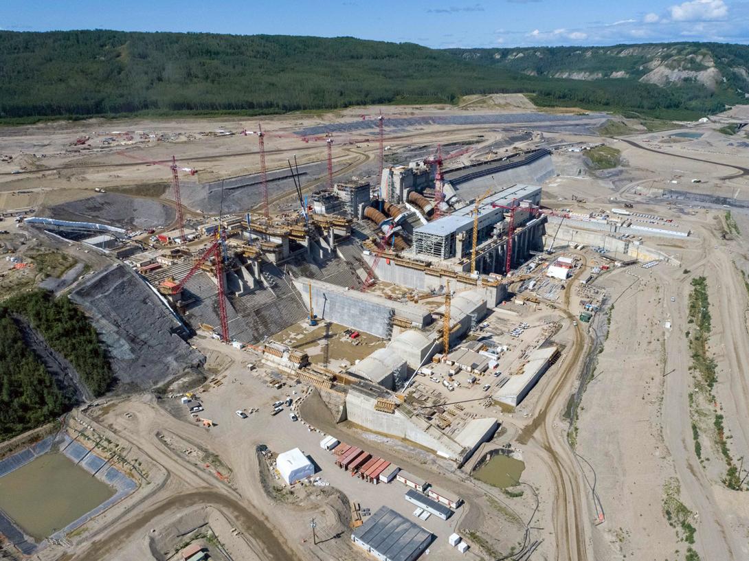 Spillway and powerhouse construction are ongoing with the Roller-Compacted Concrete (RCC) Buttress and the approach channel in the background. | July 2021