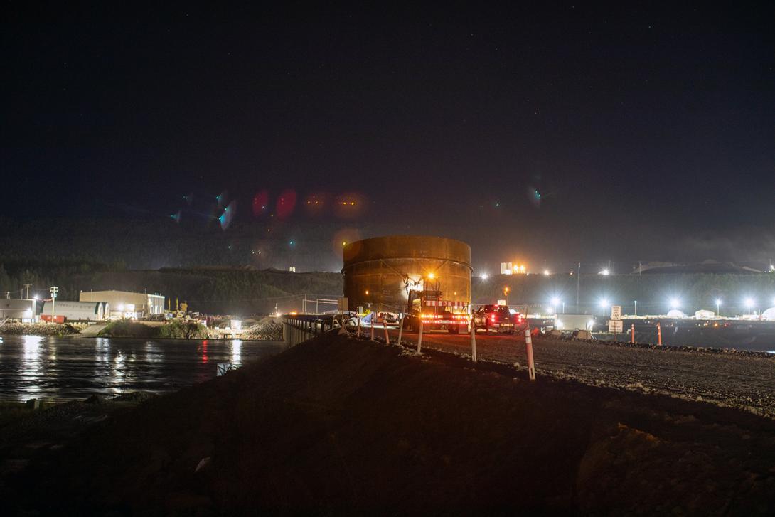 A penstock segment travels across the temporary Peace River construction bridge to its final destination at the powerhouse. | August 2019