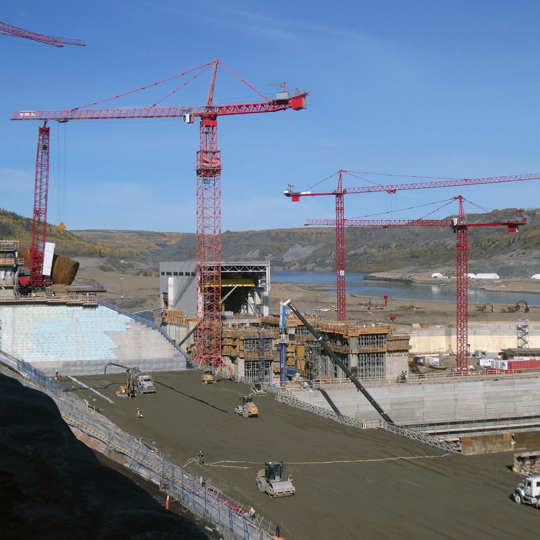 Roller-compacted concrete is placed on the spillway buttress, with the powerhouse in the background. | September 2019