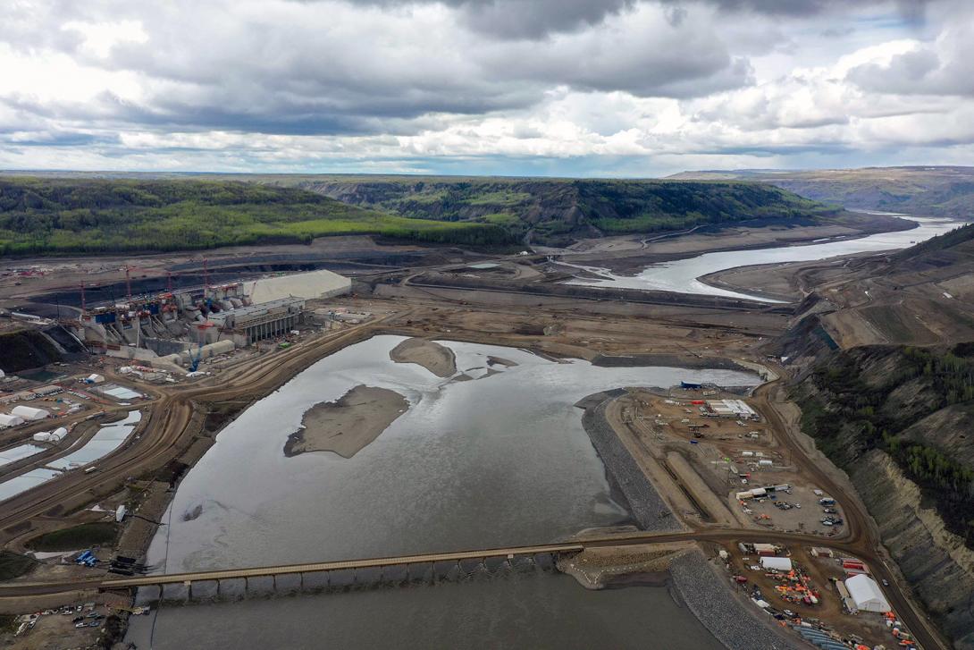 An upstream view of the powerhouse and generating station, with laydown areas, temporary fishway and outlet portals. | May 2022
