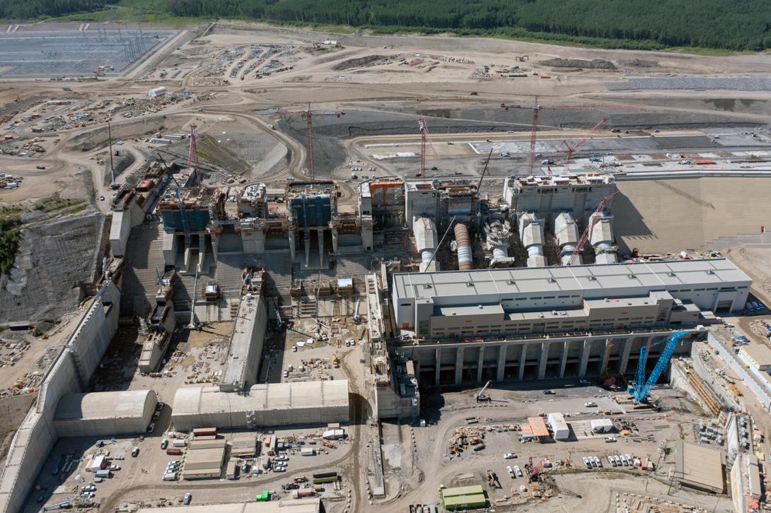 Aerial view over the spillways and stilling basin, with the penstocks behind the powerhouse and operations building. | July 2022