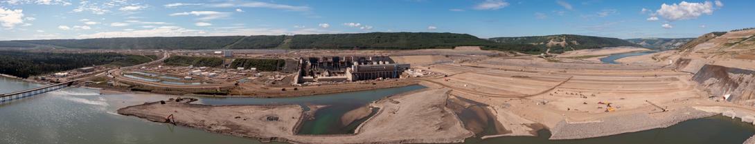 Panorama view of the powerhouse and generating station at left centre with the dam under construction at right centre. Excavators source aggregate from the river in front of the dam. | July 2022