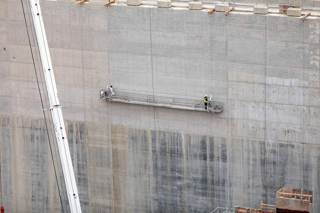 Workers use a swing stage to patch and finish concrete on a spillway training wall. | November 2022