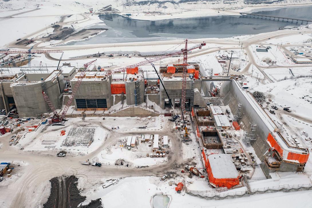 Crews work on the interior wall of the passive spillway (at right), which is like an overflow spillway. Under the orange tarps at centre, crews install the second spillway operating gate. | January 2023