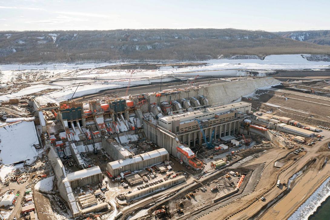 Water will exit the generating station to the tailrace and flow downstream. At left, construction is underway on the spillways. | March 2023