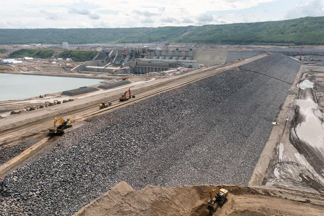 Facing the right bank across the upstream side of the dam where riprap has been placed to protect the dam. The permanent debris management ramp is being built at bottom.