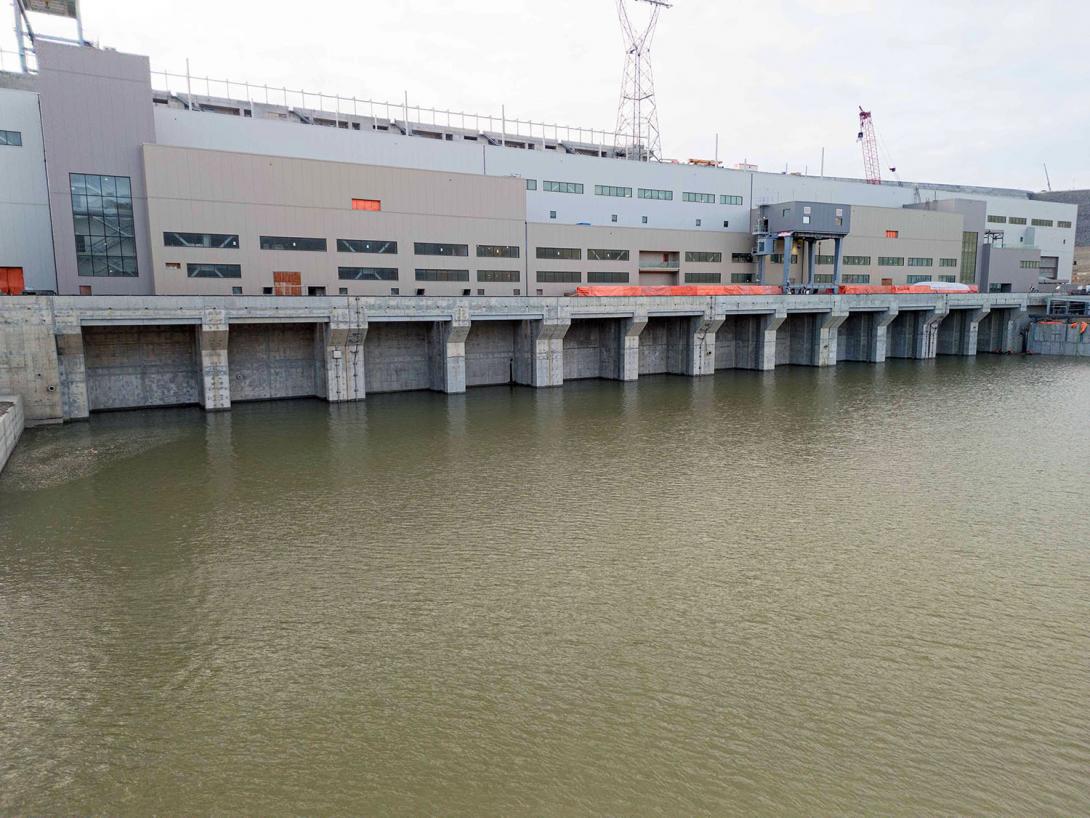 The powerhouse and operations buildings with the 12 tailrace gate openings partially covered by the tailrace pool. | November 2023