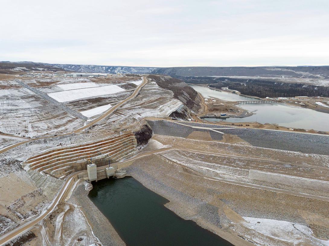 The Peace River enters the diversion inlet portal at bottom left of the completed dam. Coconut matting covered with snow is part of early reclamation work on the north bank. | November 2023