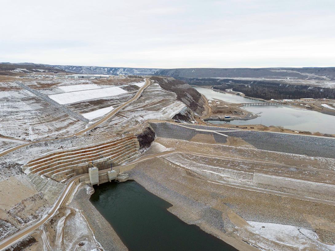 The Peace River enters the diversion inlet portal at bottom left of the completed dam. Coconut matting covered with snow is part of early reclamation work on the north bank. | November 2023
