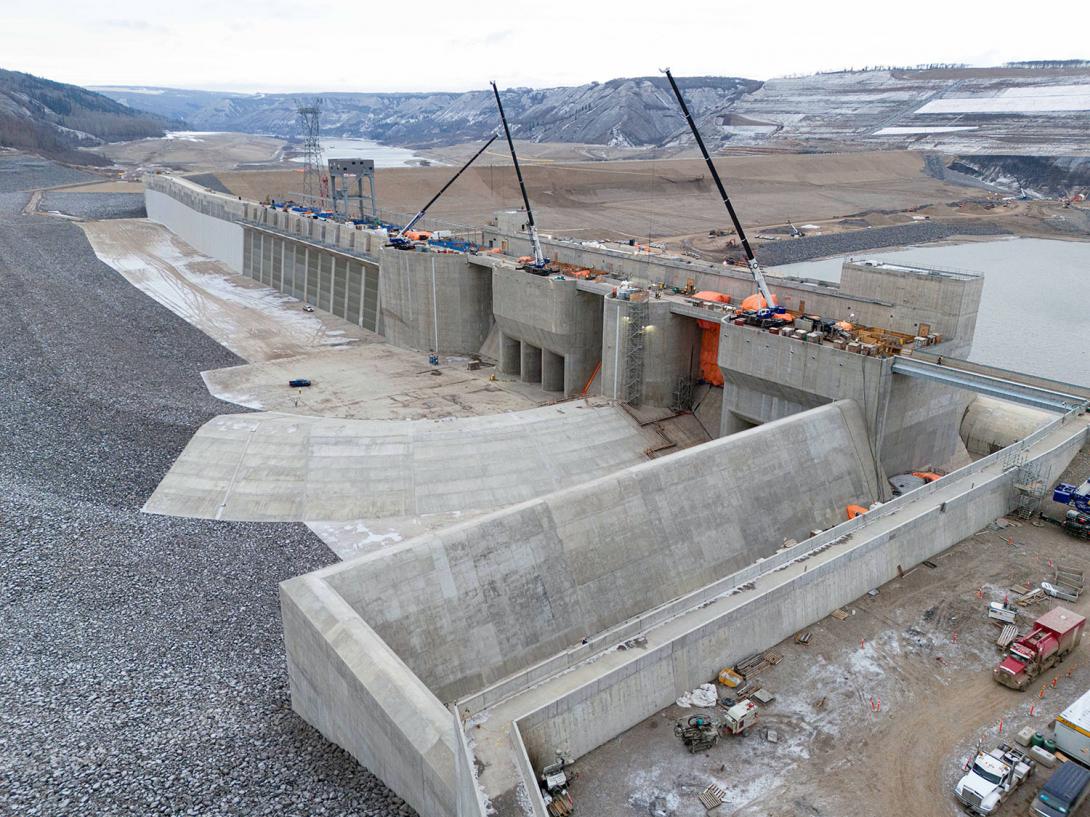 The approach channel is completed. Water will flow down the channel and enter the intakes, where trash racks have been installed. The auxiliary spillway channel is seen in the foreground. | November 2023
