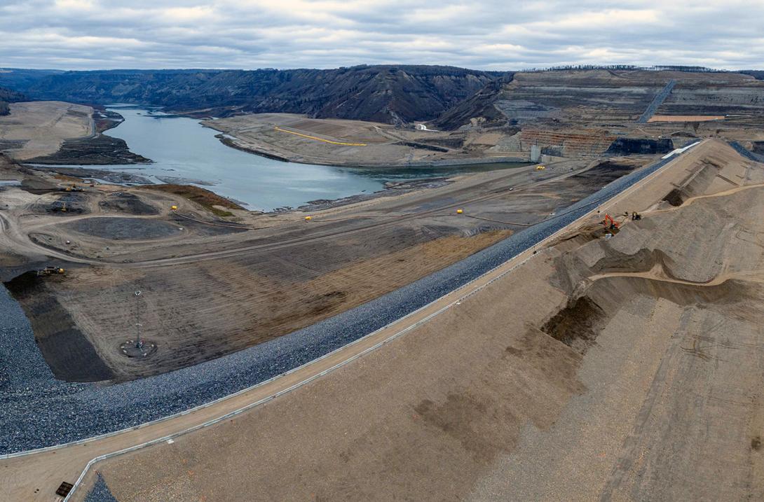 Rip rap placement is completed on the reservoir side of the earthfill dam. There is a service road on the downstream side.