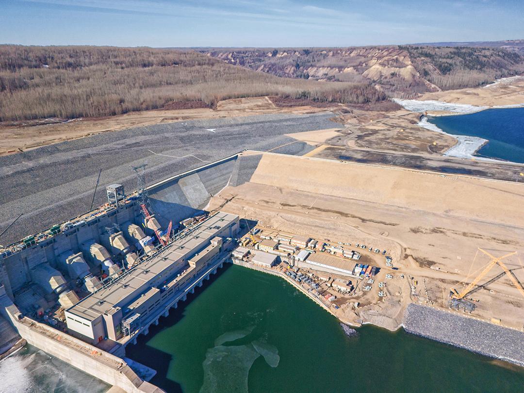 The Moberly River at top right flows into the Peace River upstream of the completed dam. The completed approach channel delivers water through the intake end of the penstocks to drop 80-metres into the powerhouse where the water turns turbine units to generate electricity. | March 2024