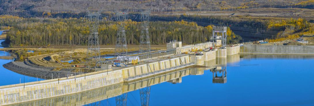 The upstream side of the intake deck. From left, the dam buttress, the six intakes, and the spillways, with the passive spillway at the end. The three transmission towers sit on penstock units 1, 3, and 5. | October 2025