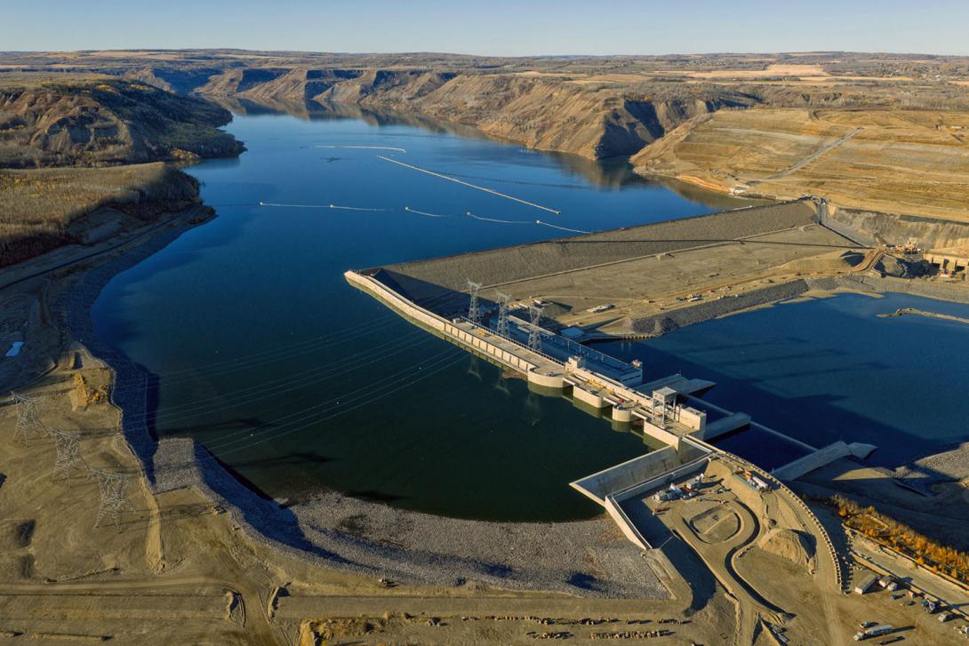 An upstream view of Site C facing northeast over the approach channel, spillways, intakes, and buttress, with the earthfill dam at the centre. | October 2025